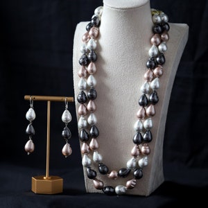 May include: A double strand pearl necklace with black, white, and pink pearls. The necklace is displayed on a white mannequin. Matching pearl earrings are displayed on a gold stand.