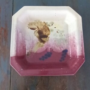 May include: A square ceramic serving dish with an octagonal rim. The dish has a white background with a brown and yellow abstract design and a burgundy bottom with blue accents.