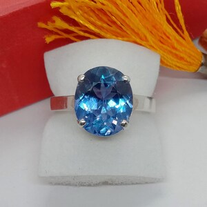 Puede incluir: Un anillo de plata con una gran piedra preciosa azul de forma ovalada. La piedra preciosa tiene un corte facetado y brilla a la luz.
