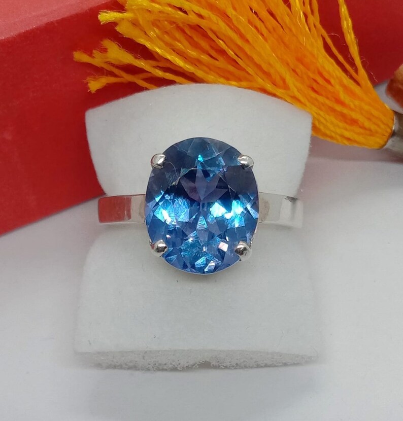 Puede incluir: Un anillo de plata con una gran piedra preciosa azul de forma ovalada. La piedra preciosa tiene un corte facetado y brilla a la luz.