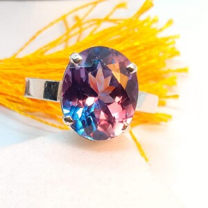 Puede incluir: Un anillo de plata con una gran piedra preciosa redonda y facetada. La piedra preciosa es una mezcla de morado, azul y rosa.