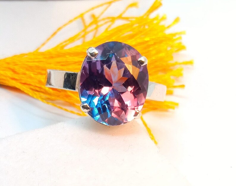 Puede incluir: Un anillo de plata con una gran piedra preciosa redonda y facetada. La piedra preciosa es una mezcla de morado, azul y rosa.