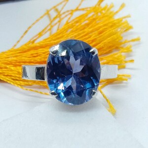Puede incluir: Un anillo de plata con una gran piedra preciosa redonda azul. La piedra preciosa tiene un corte facetado y est&aacute; engastada en un engaste de garras.