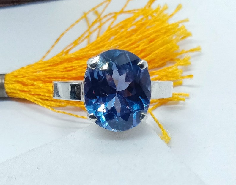 Puede incluir: Un anillo de plata con una gran piedra preciosa redonda azul. La piedra preciosa tiene un corte facetado y est&aacute; engastada en un engaste de garras.