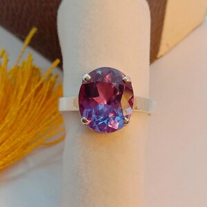 Puede incluir: Un anillo de plata con una gran piedra preciosa de forma ovalada. La piedra preciosa es de color morado oscuro que se desvanece a un azul m&aacute;s claro en la parte inferior. El anillo est&aacute; engastado con cuatro peque&ntilde;as garras de plata.