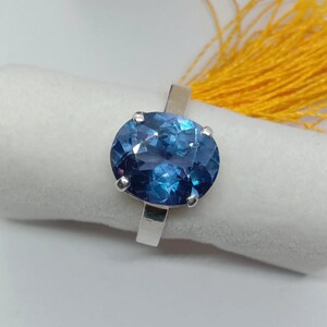 Puede incluir: Un anillo de plata con una gran piedra preciosa azul de forma ovalada. La piedra preciosa tiene un corte facetado y un color azul profundo.