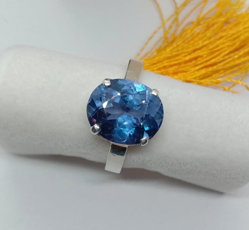 Puede incluir: Un anillo de plata con una gran piedra preciosa azul de forma ovalada. La piedra preciosa tiene un corte facetado y un color azul profundo.