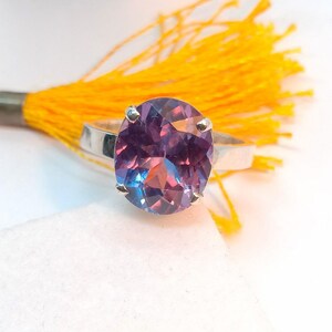 Puede incluir: Un anillo de plata con una gran piedra preciosa ovalada de color p&uacute;rpura y azul. La piedra preciosa tiene un corte facetado y est&aacute; engastada en una banda simple.
