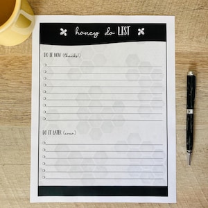 May include: A black and white "honey do LIST" notepad with bee graphics. The notepad has sections for "Do it now" and "Do it later" with lined spaces. A black pen rests on the right side of the notepad. A yellow mug is in the upper left corner.
