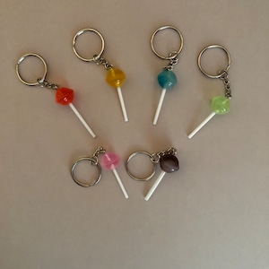 May include: Six colorful lollipop keychains with silver key rings. The lollipops are pink, orange, yellow, blue, green, and brown.