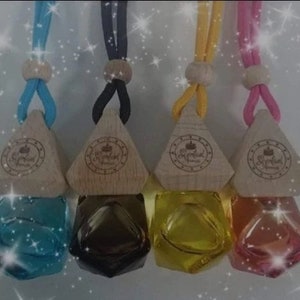 May include: Four diamond-shaped car air fresheners with wooden tops and glass bottles. The wooden tops have a logo that says "Sophisticated Scents". The bottles are filled with different colored liquids: blue, black, yellow, and pink.