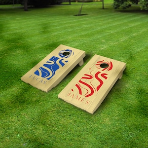 May include: Two wooden cornhole boards with personalised names, "Lucas" and "James". Each board features a unique abstract design with blue and red wavy lines.