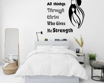 Op de afbeelding: Een witte slaapkamer met een bed, een spiegel, een nachtkastje en een plant. De muur heeft een zwart-witte vinyl sticker met de tekst "Ik kan alles door Christus, die mij kracht geeft".