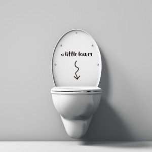 May include: White toilet bowl with a white toilet seat. The toilet seat has a black sticker with the text "a little lower" and a downward arrow.