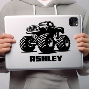 May include: A black and white illustration of a monster truck with the name "ASHLEY" printed below it. The truck has large tires and is depicted in a cartoon style.
