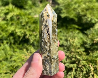 May include: A green, brown, and white crystal point with a pointed tip. The crystal has a natural, rough texture.