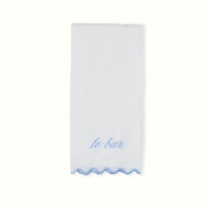 May include: White bar towel with a light blue scalloped edge and embroidered text "le bar". The towel is rectangular and made of a soft, absorbent fabric. The text is in a cursive font.