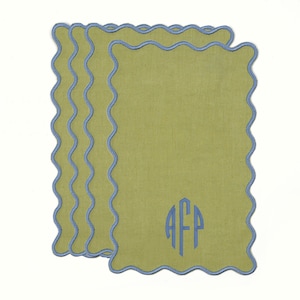 May include: A stack of four olive green rectangular cloth napkins with a wavy blue border. Each napkin has a blue monogram in the lower right corner. The napkins are on a white background.