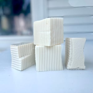 May include: Four white rectangular bars of soap stacked on top of each other. The soap has a textured surface.