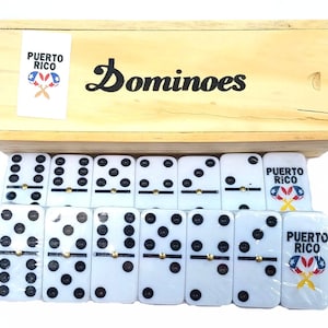 May include: A set of white dominoes with black dots, packaged in a wooden box. The box has the text "Dominoes" and a Puerto Rico flag logo with the words "Puerto Rico".