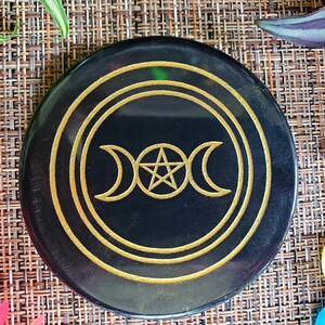 May include: Black circular stone coaster with a gold triple moon and pentagram design.
