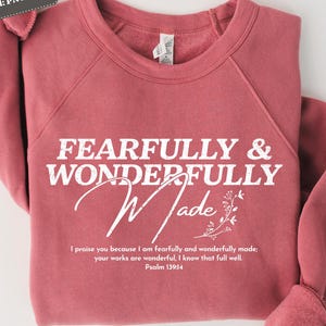 May include: A maroon sweatshirt with the text "Fearfully & Wonderfully Made" in white. The text is accompanied by a small floral design and a quote from Psalm 139:14.