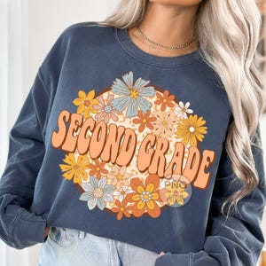May include: A navy blue sweatshirt with a retro-style graphic design featuring the text "Second Grade" surrounded by colorful flowers.