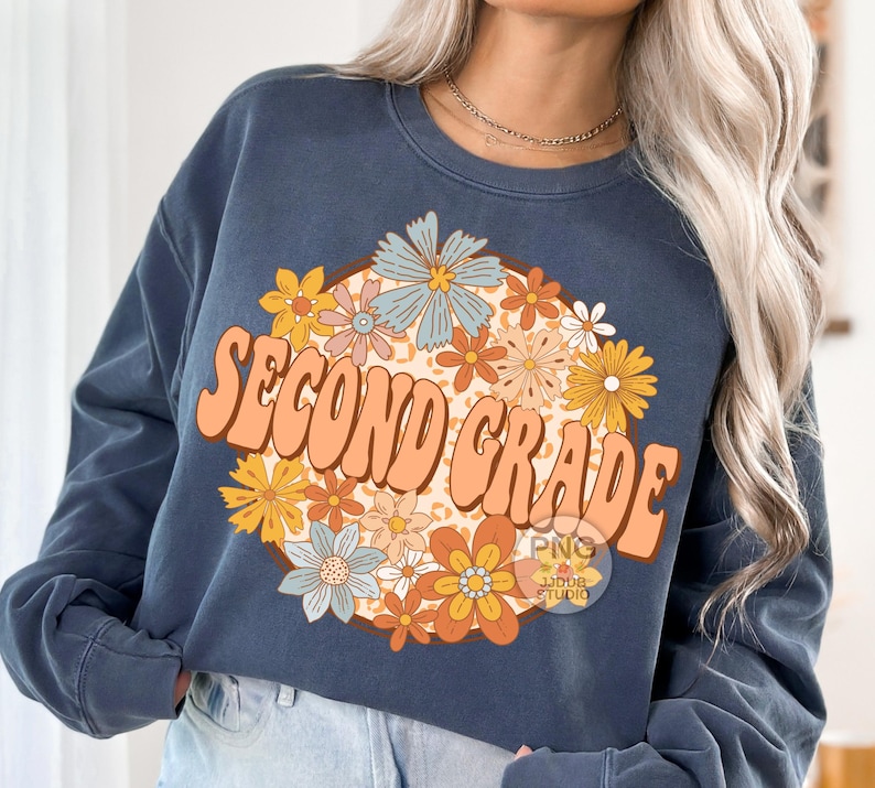 May include: A navy blue sweatshirt with a retro-style graphic design featuring the text "Second Grade" surrounded by colorful flowers.