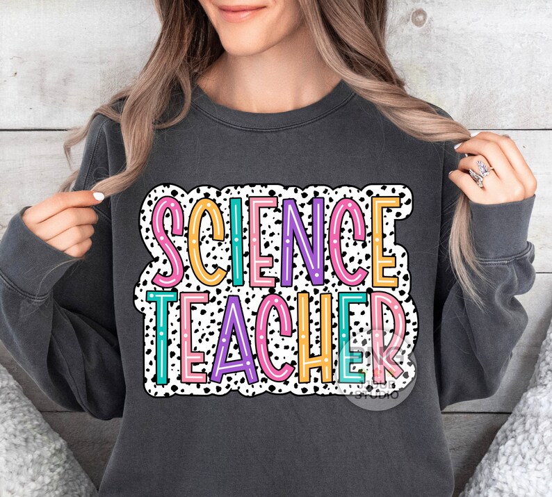 Peut inclure: Un sweat-shirt gris fonc&eacute; avec les mots "SCIENCE TEACHER" en lettres color&eacute;es sur un fond de pois blancs et noirs.