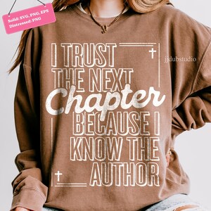 以下が含まれることがあります： 「I TRUST THE NEXT Chapter BECAUSE I KNOW THE AUTHOR」の白文字がプリントされた茶色のスウェットシャツ。デザインには十字架が含まれています。スウェットシャツはクルーネックと長袖です。