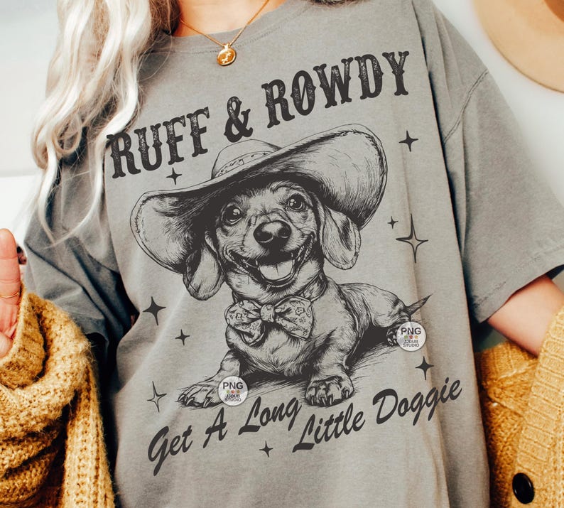 May include: A gray t-shirt with a black and white illustration of a dachshund wearing a cowboy hat. The text "Ruff & Rowdy" is above the dog and "Get A Long Little Doggie" is below the dog.