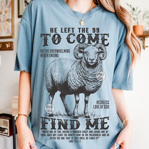 May include: A pale blue t-shirt with a detailed illustration of a ram. The shirt features the text "HE LEFT THE 99 TO COME" and "FIND ME", along with a quote from Luke 15:3-7. The design is in black and white.