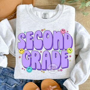 May include: A light grey sweatshirt with the text "Second Grade" in purple with a 3D effect. The text is surrounded by colorful stars and smiley faces.