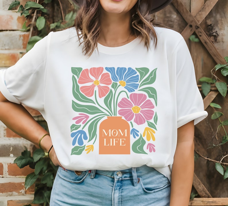 May include: White t-shirt with a floral design and the text "MOM LIFE" printed on the front. The flowers are pink, blue, and orange.