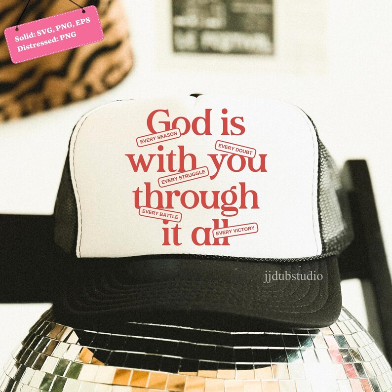 May include: A black and white trucker hat with the text "God is with you through it all" in red. The hat has a white front panel and a black brim and mesh back. The hat is sitting on a mirrored disco ball.