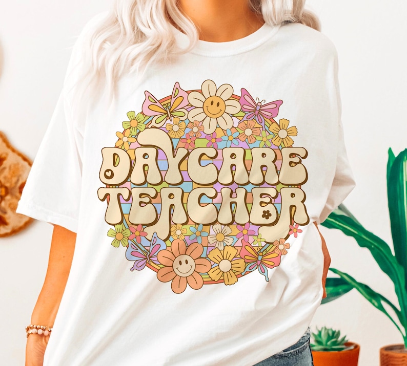 Peut inclure: T-shirt blanc avec un graphique r&eacute;tro d'un arc-en-ciel et de fleurs avec le texte "Daycare Teacher".