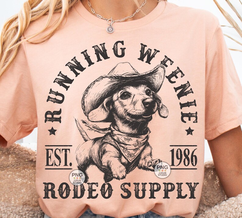May include: A peach-colored t-shirt with a black and white illustration of a dachshund wearing a cowboy hat. The text "Running Weenie Est. 1986 Rodeo Supply" is printed on the shirt.