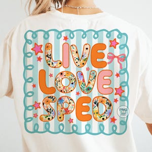 May include: White t-shirt with a colorful graphic on the back. The graphic says "LIVE LOVE SPED" in orange and pink letters, with floral patterns in some letters. The design is framed by a teal border with stars and a pink bow.