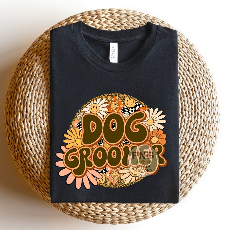 May include: Black t-shirt with a brown and orange graphic design that says "DOG GROOMER" surrounded by flowers and smiley faces.