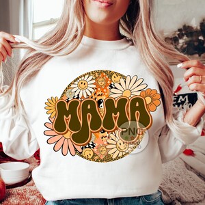 May include: White sweatshirt with a brown "MAMA" graphic in a retro font surrounded by colorful flowers and a leopard print circle.