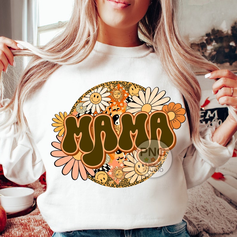 May include: White sweatshirt with a brown "MAMA" graphic in a retro font surrounded by colorful flowers and a leopard print circle.