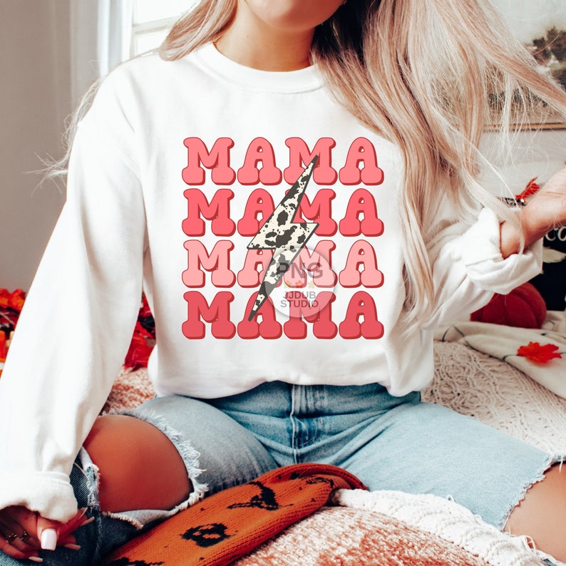 May include: White sweatshirt with a pink and red retro-style graphic that says "Mama" four times with a cow print lightning bolt in the center.