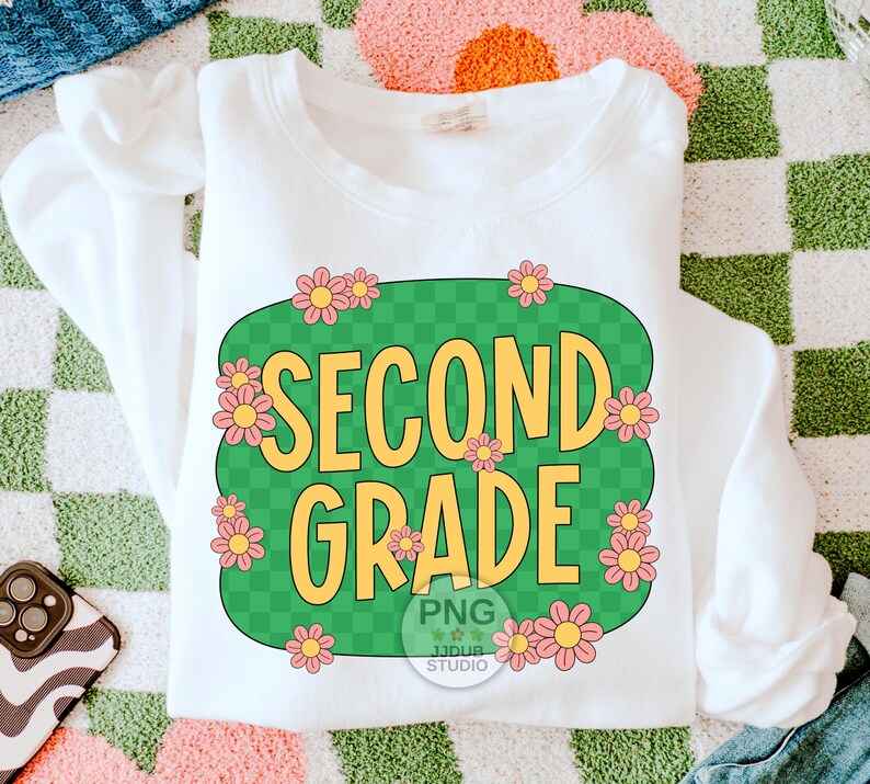 May include: White sweatshirt with a green and white checkered design featuring the text "Second Grade" in yellow letters surrounded by pink flowers.