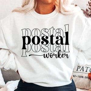 May include: White sweatshirt with black text that reads "postal worker" in a layered, stacked font style.