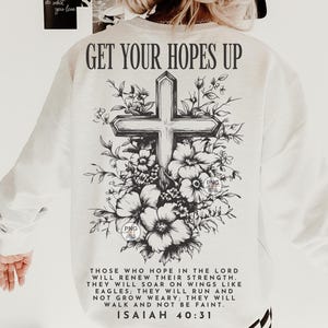 Peut inclure: Sweat-shirt blanc avec un motif graphique noir et blanc d'une croix entour&eacute;e de fleurs. Le texte "GET YOUR HOPES UP" est en haut du motif. Le texte "THOSE WHO HOPE IN THE LORD WILL RENEW THEIR STRENGTH. THEY WILL SOAR ON WINGS LIKE EAGLES; THEY WILL RUN AND NOT GROW WEARY; THEY WILL WALK AND NOT BE FAINT. ISAIAH 40:31" est en bas du motif.