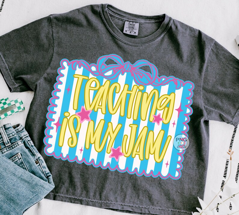 以下が含まれることがあります： 「TEACHING IS MY JAM」の黄色い文字が、青と白のストライプの背景に描かれた濃いグレーのTシャツ。ピンクの星とリボンがデザインされています。Tシャツは青いジーンズと組み合わせています。