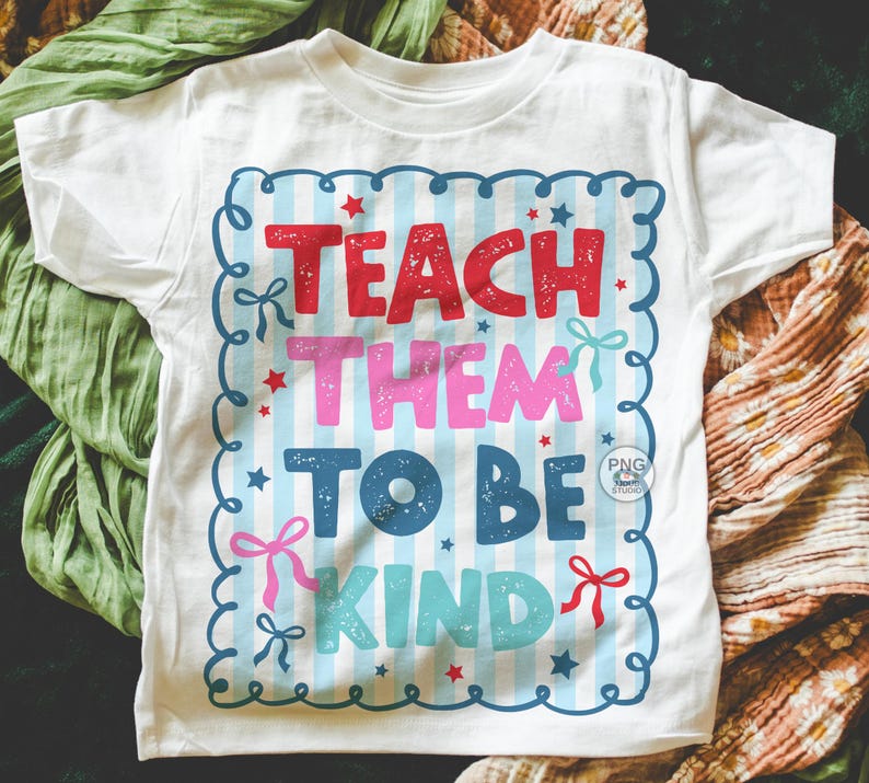 以下が含まれることがあります： 赤、ピンク、青、ターコイズ色の「TEACH THEM TO BE KIND」という文字がプリントされた白いTシャツ。テキストは、リボンと星が付いた青と白のストライプのフレーム内にあります。シャツは柔らかい素材で作られています。
