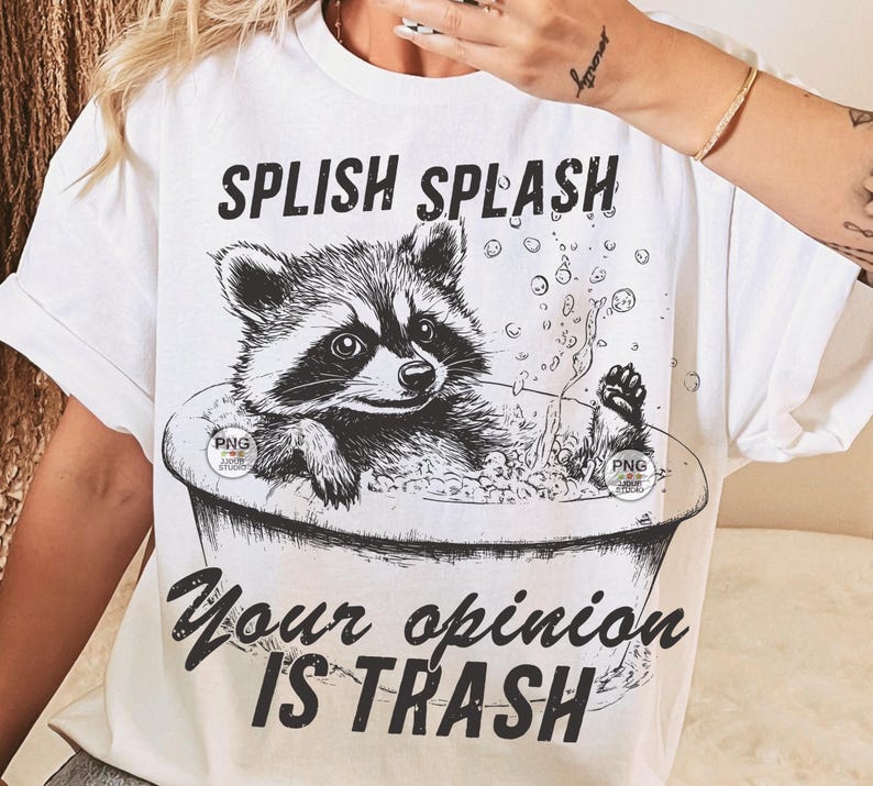 K&ouml;nnte beinhalten: Wei&szlig;es T-Shirt mit einer schwarz-wei&szlig;en Illustration eines Waschb&auml;ren in einer Badewanne mit Blasen. Der Text "Splish Splash Your Opinion Is Trash" ist auf das T-Shirt gedruckt.
