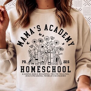 May include: A beige sweatshirt with a black graphic design that says "Mama's Academy" with a stack of books and flowers. The text below the graphic says "PR. 22:6 Homeschool Raising Bible Reading, Truth Telling, Jesus Praising, World Changers!"