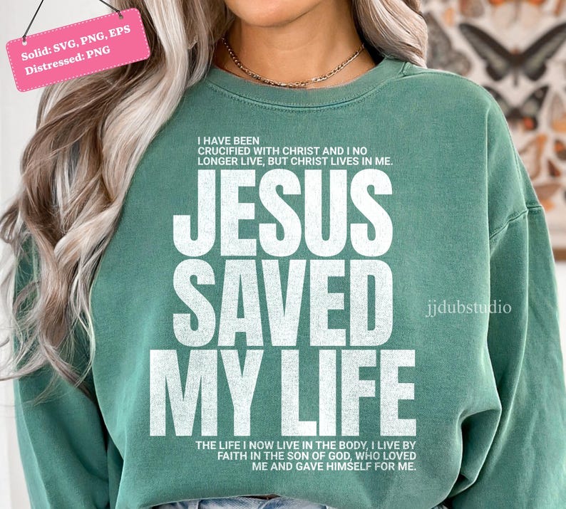Może przedstawiać: Zielona bluza z napisem "JESUS SAVED MY LIFE" dużymi białymi literami. Bluza ma r&oacute;wnież dodatkowy tekst nad i pod gł&oacute;wnym wyrażeniem. Projekt jest postarzany, co nadaje mu wygląd vintage.